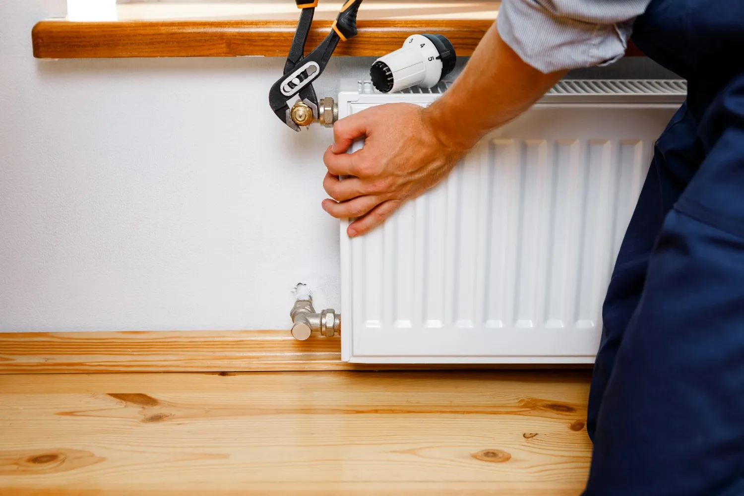 Technicien installant ou réparant un radiateur de chauffage sur un parquet.